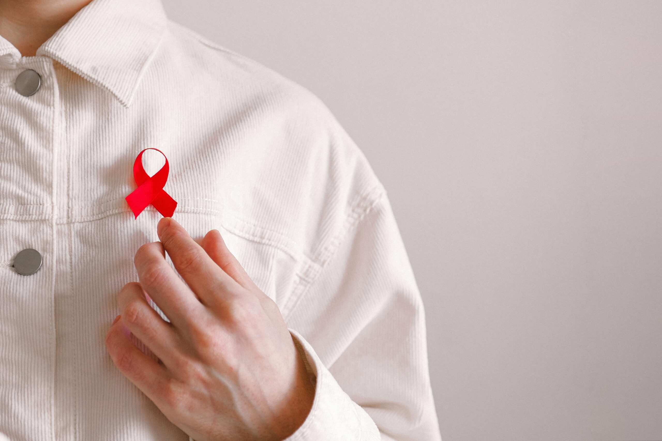 A person touching the red HIV ribbon on their white shirt.